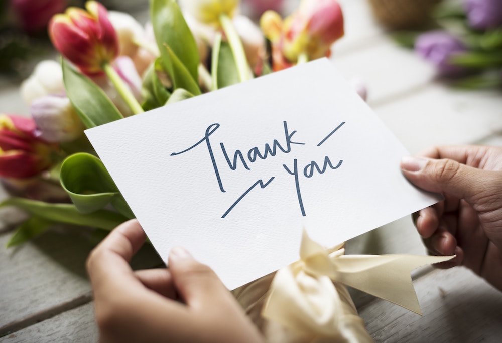 hand holding a thank you card and bouquet of flowers