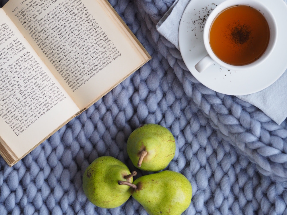 A book, cup of tea, and pears sitting on a placemat