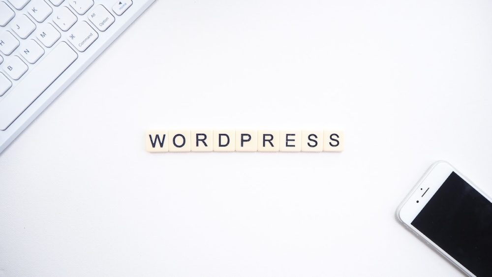 best plugins for wordpress - tiles on a desk spelling out wordpress with computer keyboard and phone nearby