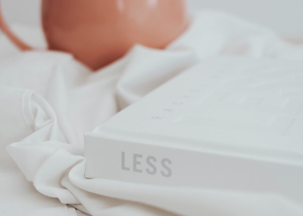 What Do You Need To Be Happy? a white book laying in the bed sheets with the word "LESS" on the spine