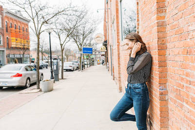 mindful self compassion: woman standing downtown against a brick wall looking downward