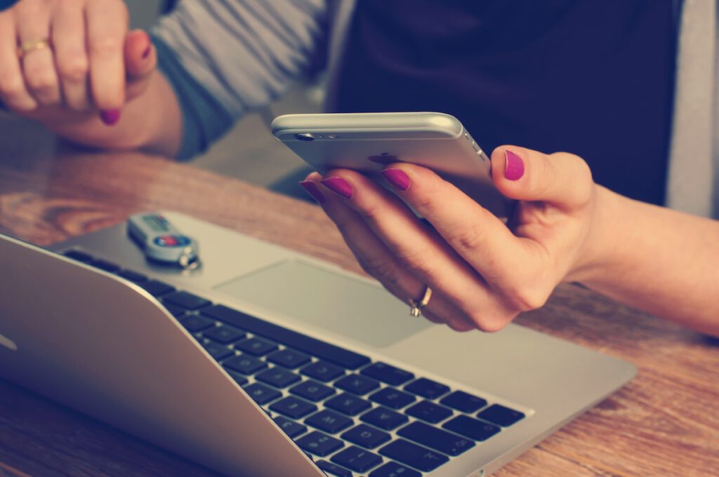 make website mobile friendly: woman sitting at her laptop with her phone in the hand