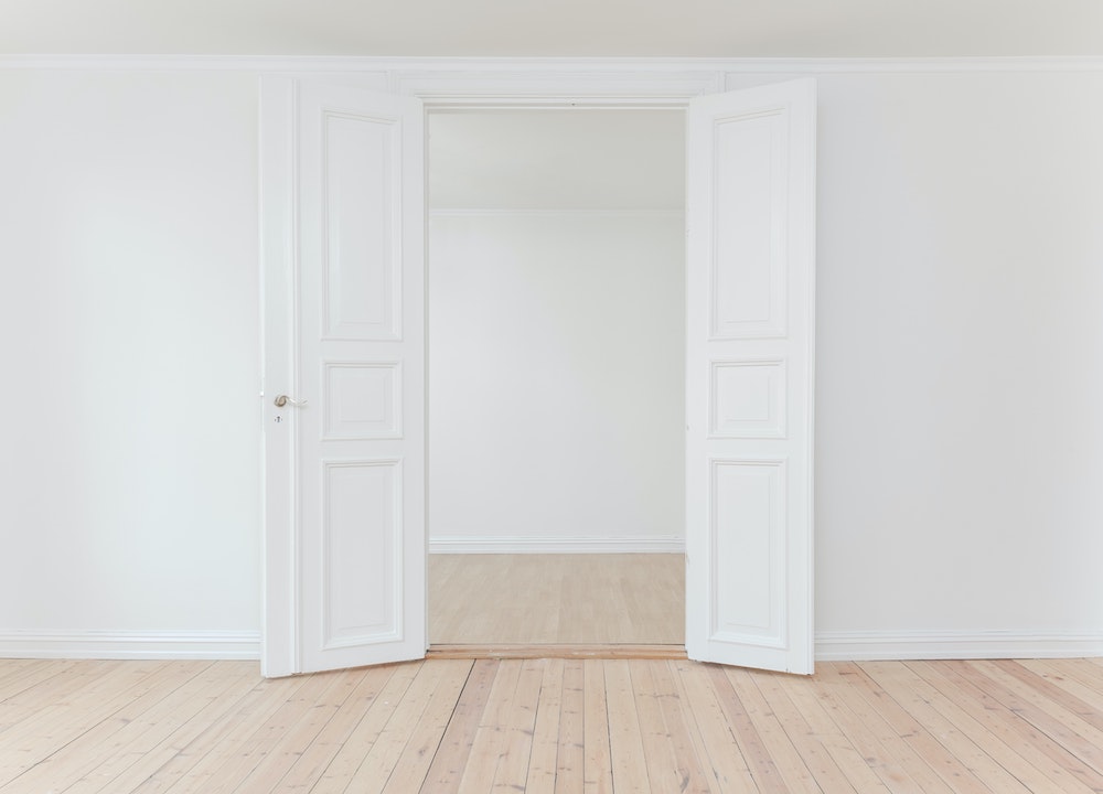 Begin living a minimalist lifestyle - two white doors opening up to an empty white room