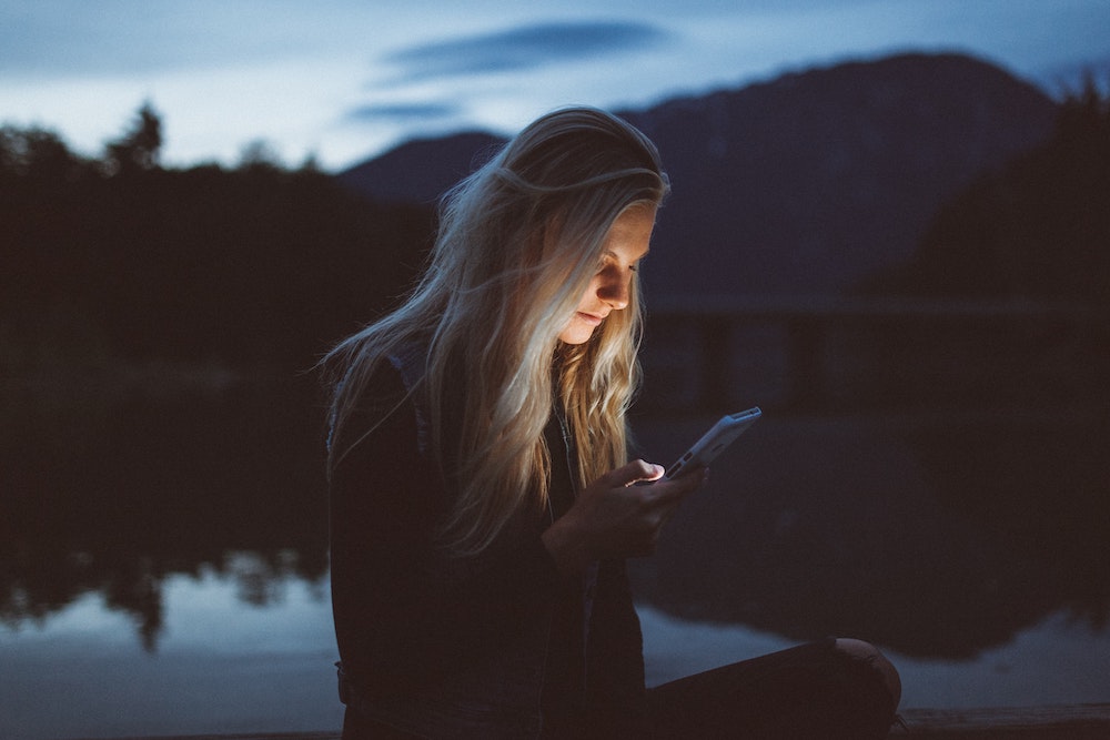 Should I delete my Facebook? Woman in a beautiful natural setting looking at her phone looking anxious