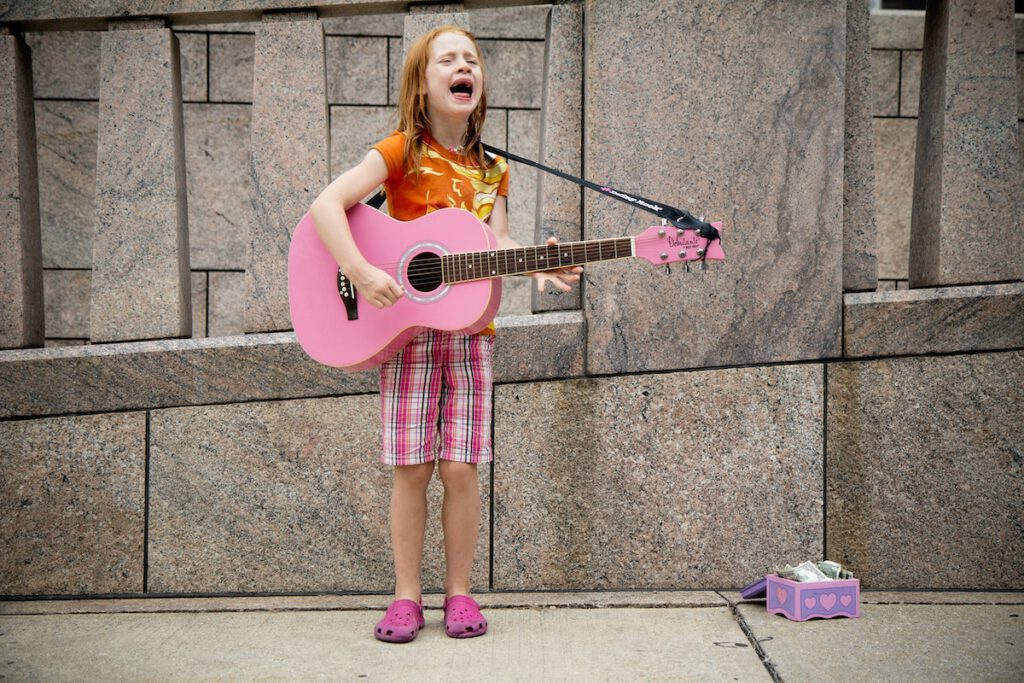 little girl singing and playing guitar on the street for money