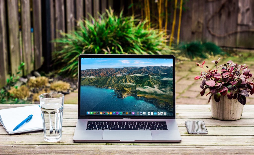 laptop on an outdoor table with flowers, glass of water, sunny day