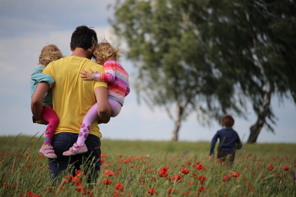 father walking with young children in a field of poppies on a summer's day