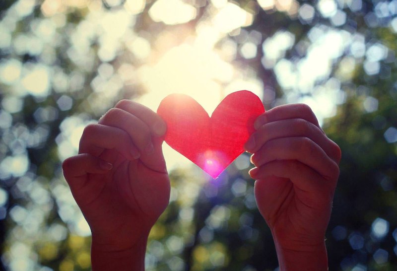 hands holding up a paper heart in the sunlight