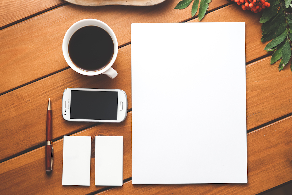 a desk with a cup of coffee, notebook, pens, and phone