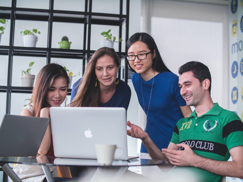 happy people gathered around a laptop smiling