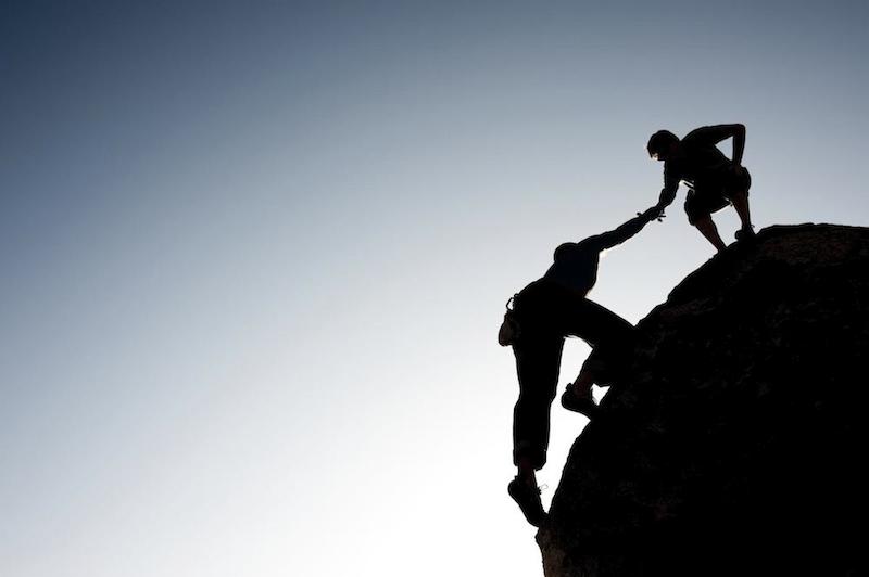 person helping another person up a mountain