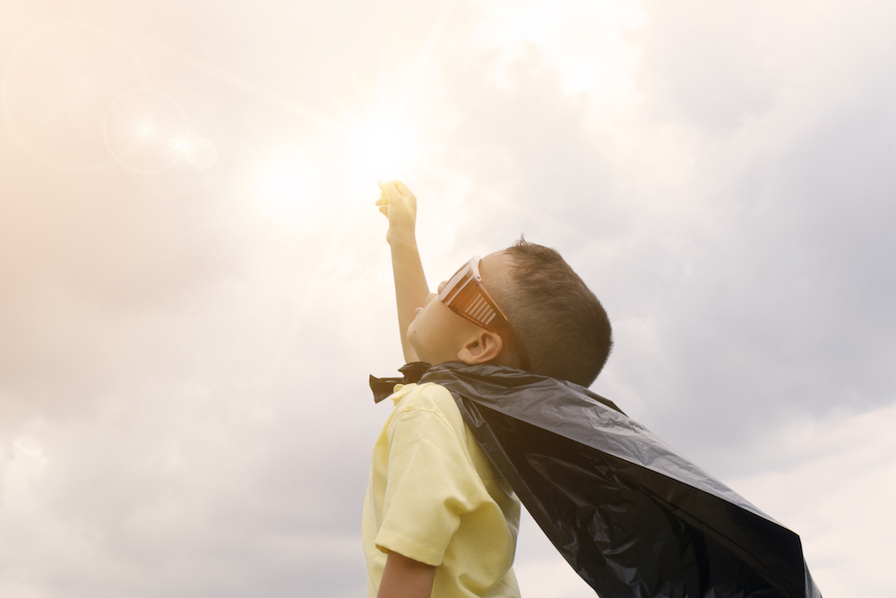 little boy with a superhero cape on and his fist pointed to the sky