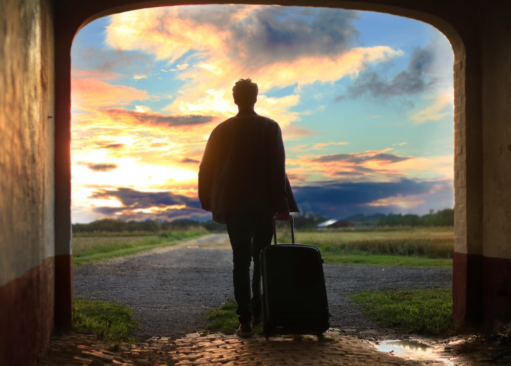 travel tips and tricks: woman heading into a sunset pulling a suitcase