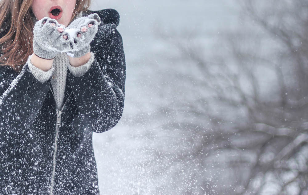 a woman in the snow blowing snowflakes from her hands